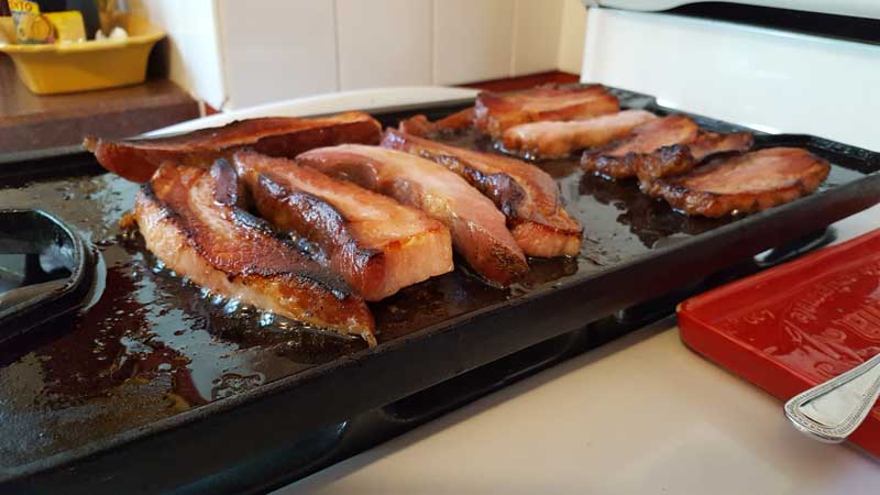 Thick slices of bacon frying