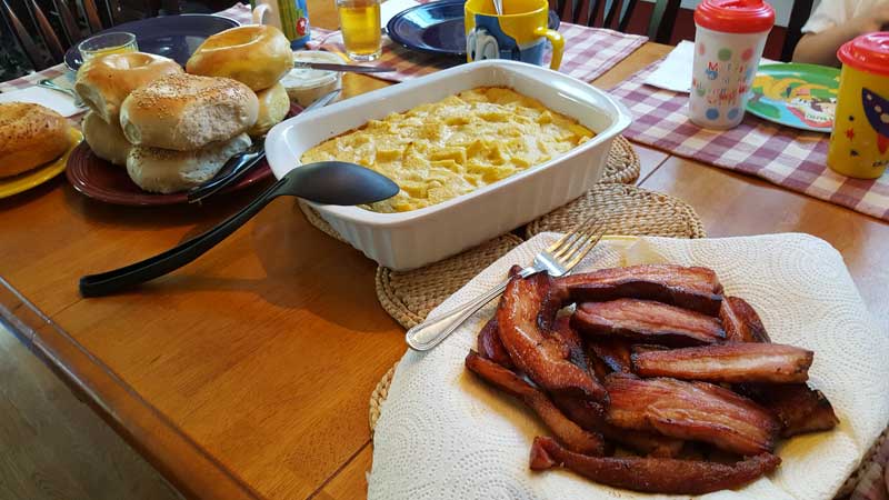 Table set with bagels, souffle, and thick sliced bacon.