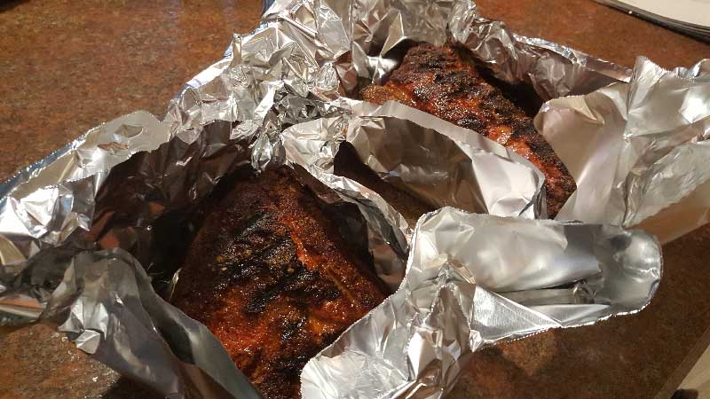 Cooked baby back ribs in a foil package.
