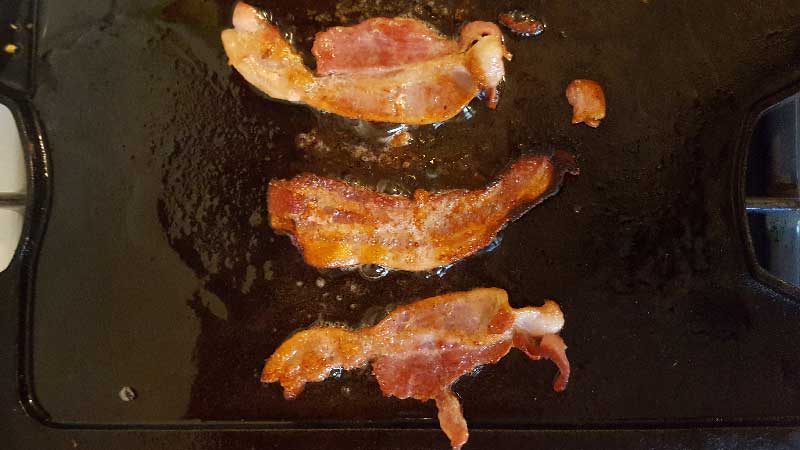 Bacon frying on a griddle.