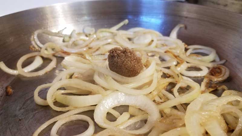 Scoop of brown sugar in the middle of frying onions in a pan.