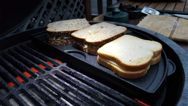 Three uncooked grilled cheese sandwiches on a griddle on the Big Green Egg.