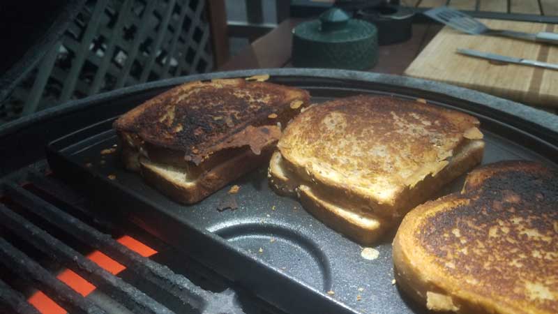 Three cooked grilled cheese sandwiches on a griddle on the Big Green Egg.