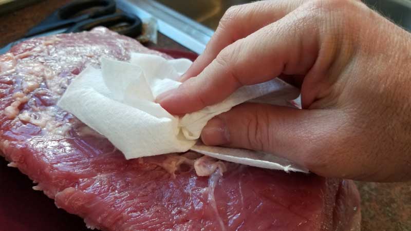 Corned beef being pat dry with a paper towel.