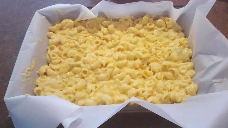 Mac and cheese in a 9 inch by 13 inch pan with parchment paper.