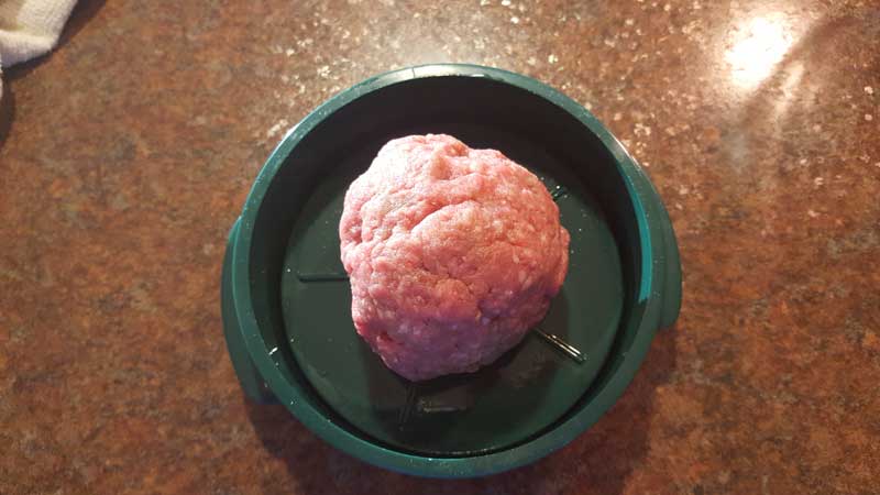 Ball of chopped meat in a burger press.