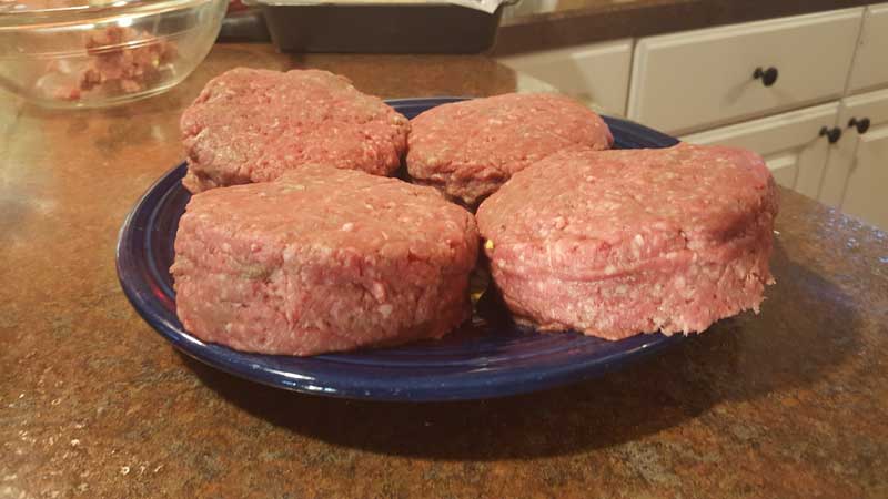 Four completed stuffed burgers on a plate.