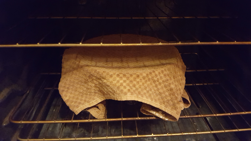 Bowl covered by a towel in an unlit oven.