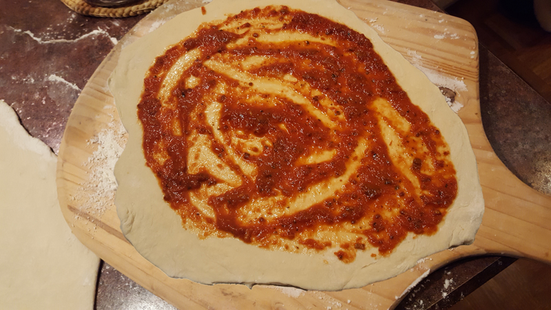 Sauce spread out on pizza dough.