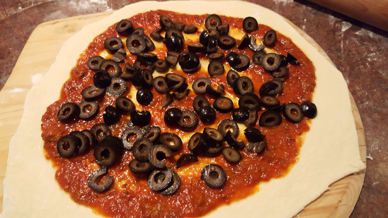 Raw pizza dough covered in sauce and black olives.