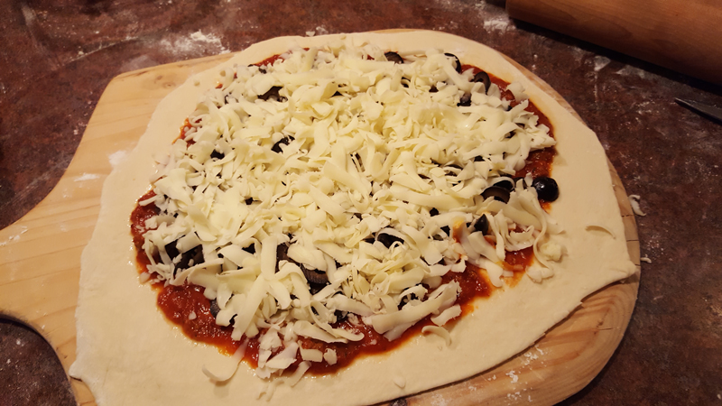 Raw pizza dough covered in sauce, olives, and grated cheese.
