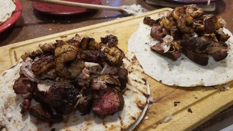 Steak, chicken, and shrimp piled on top of tortilla.