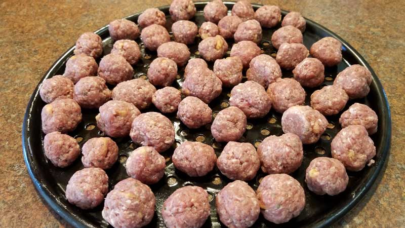 Uncooked meatballs on perforated tray.