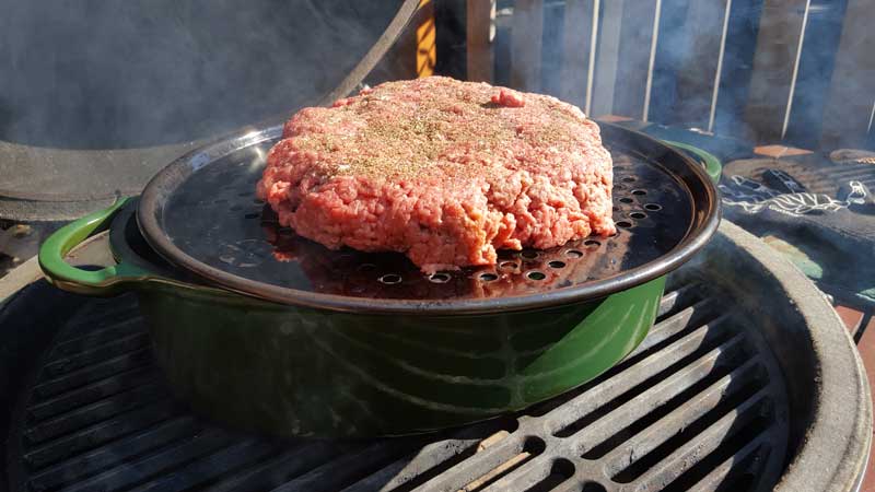 Large beef patty sitting on top of a cooking grid on top of a dutch oven.